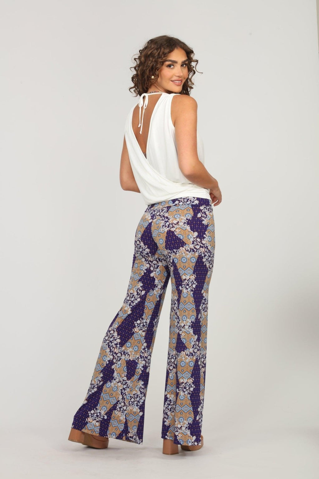 back side of white sleeveless blouse and multicolored, printed, wide-legged pants on woman