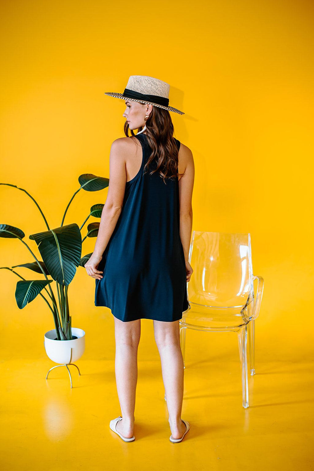 back side of navy sleeveless short dress on woman with yellow background