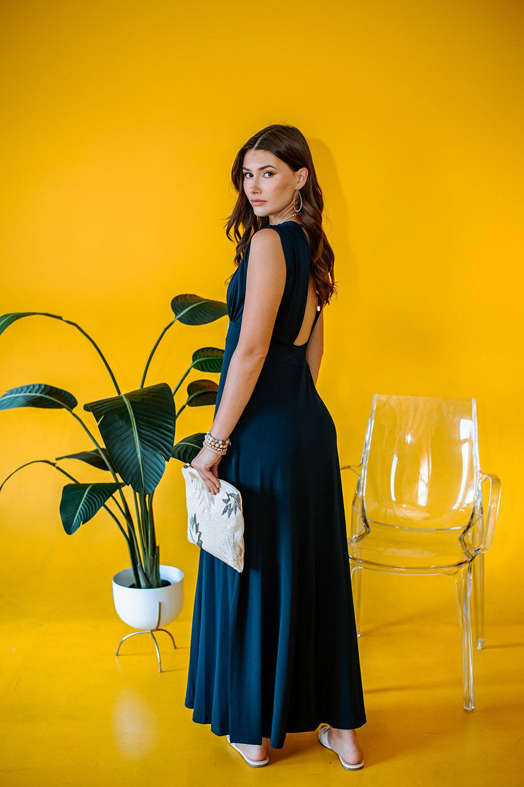backside of navy sleeveless maxi dress with deep neckline and side slit on woman with yellow background