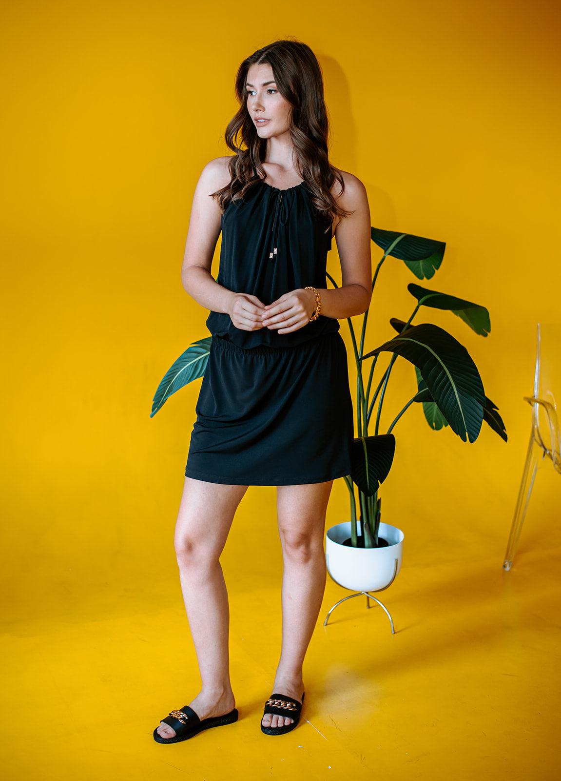 black sleeveless halter dress on woman in black sandals with yellow background