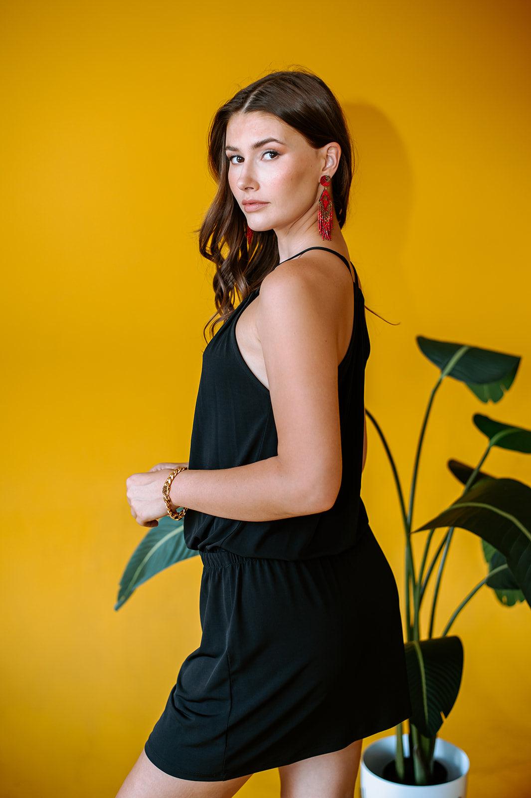 back side of black sleeveless halter dress on woman with yellow background