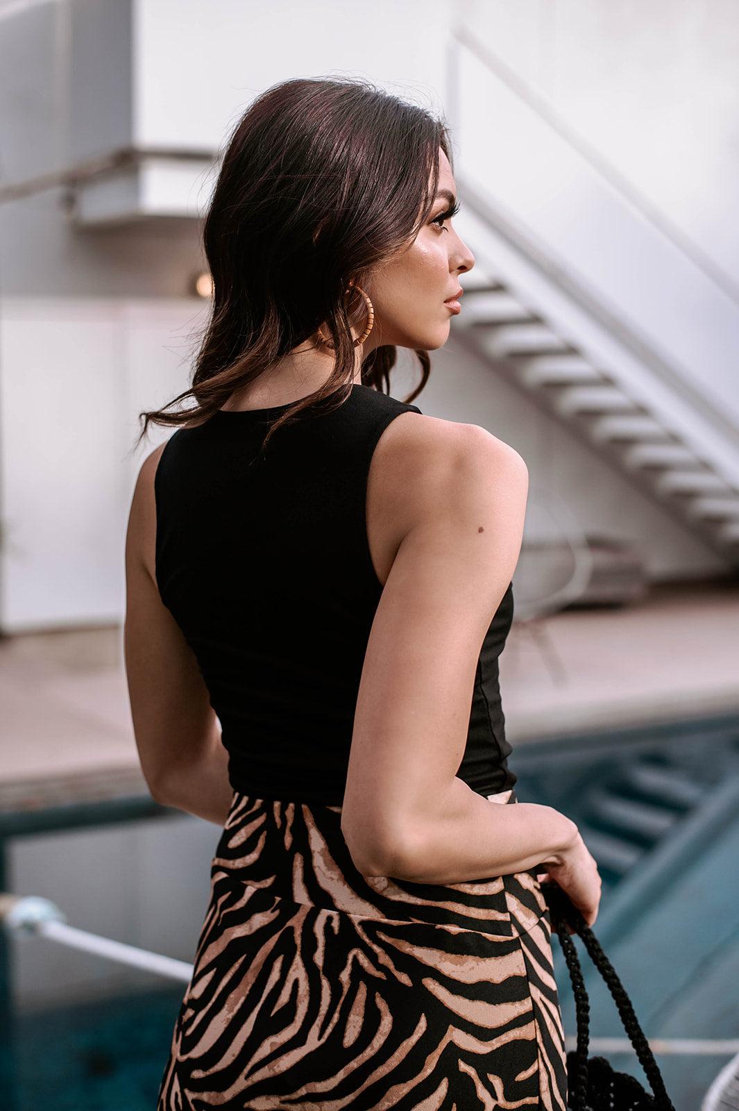back side of black sleeveless cropped top and animal print skirt on woman