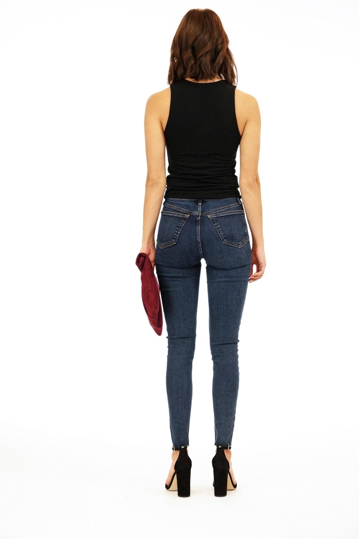 back side of black sleeveless cropped top and dark denim pants on woman in black heels