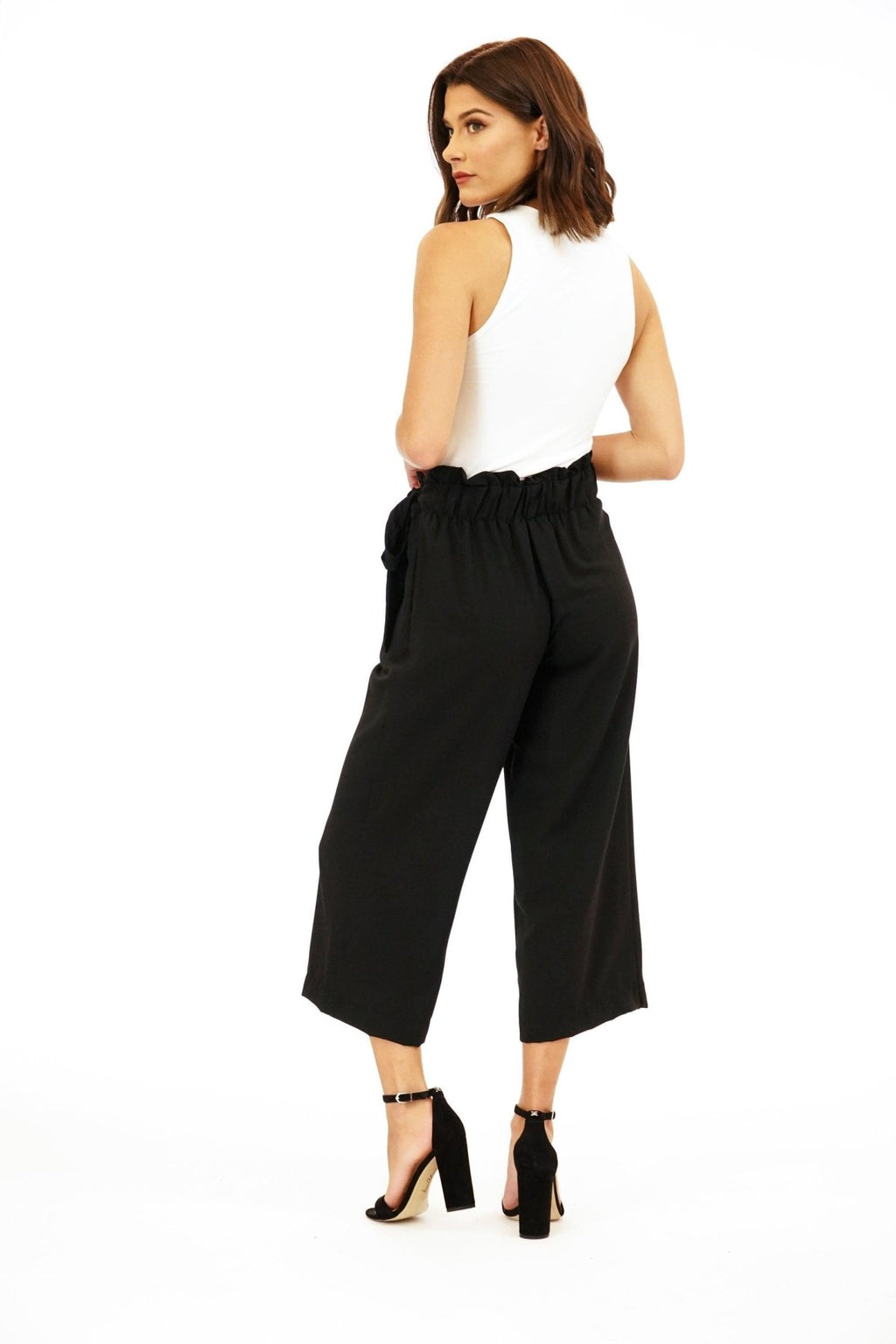 back side of white sleeveless top on woman in black pants and black high heels