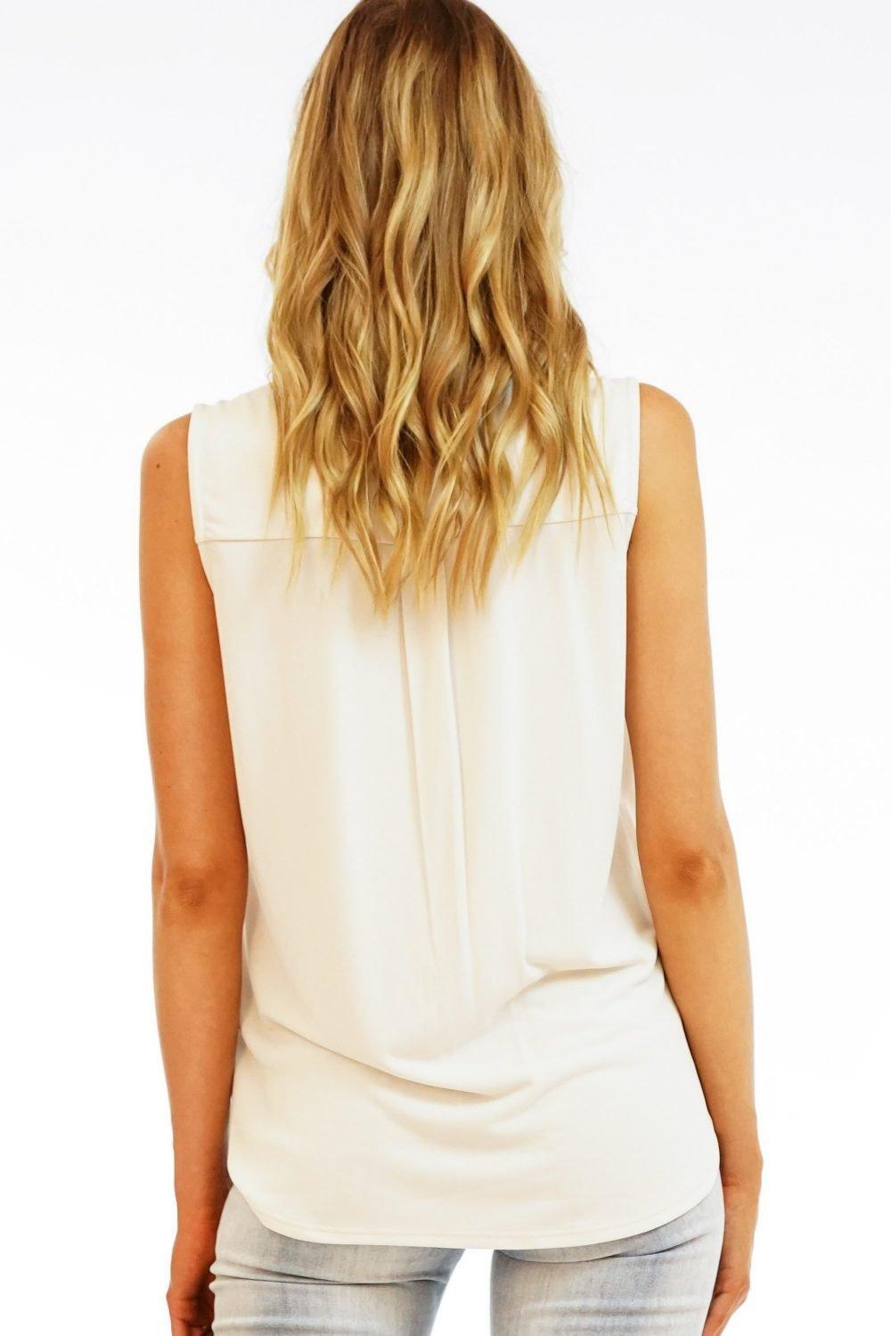 back side of beige sleeveless blouse on woman in light denim pants