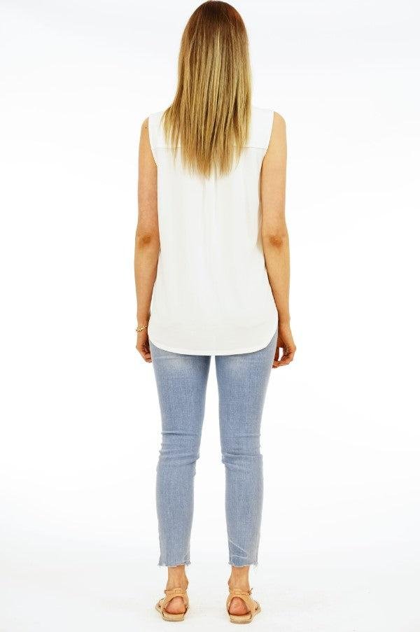 back side of ivory sleeveless blouse on woman in denim pants
