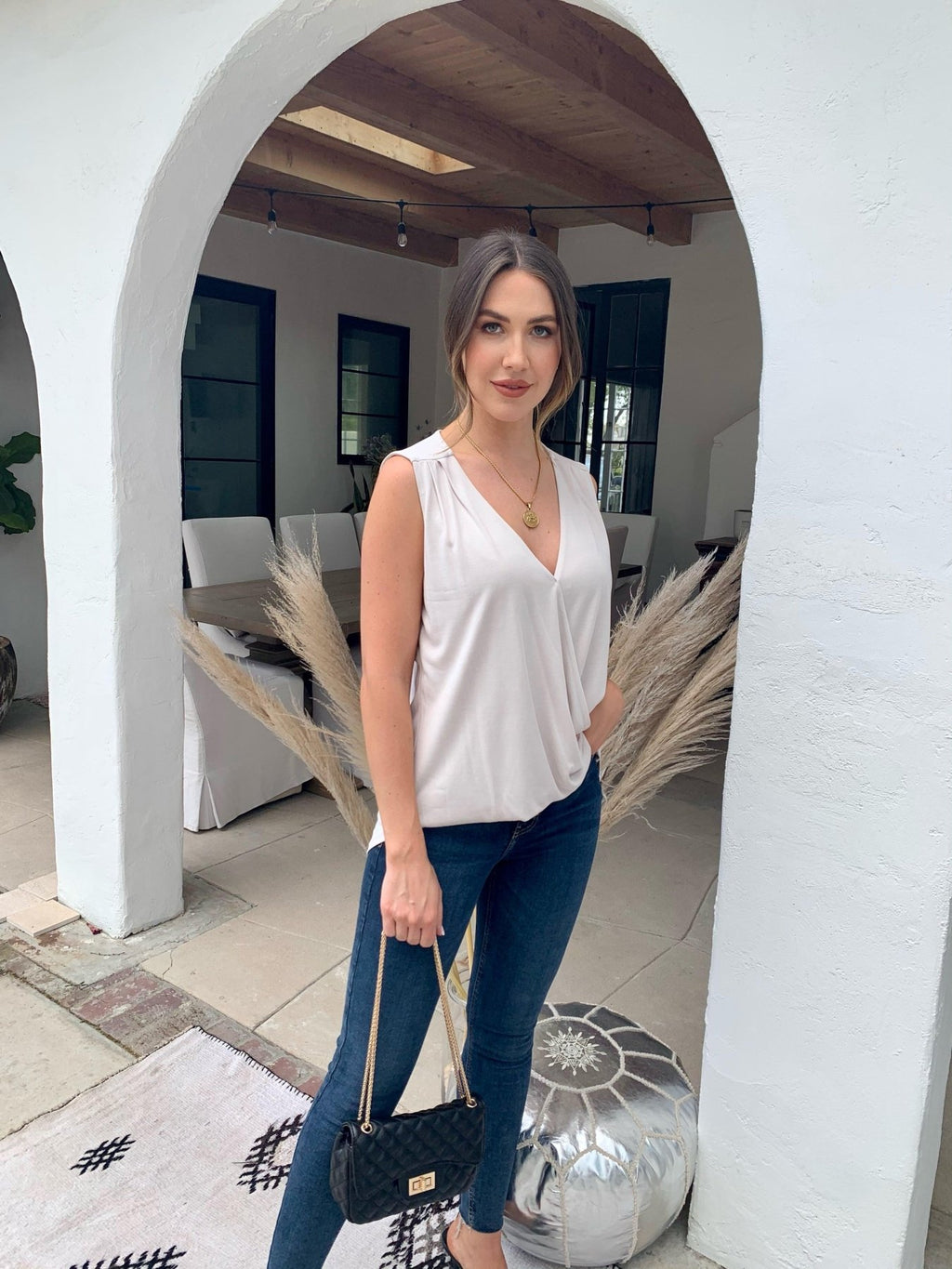 beige sleeveless blouse on woman in dark denim pants holding black purse