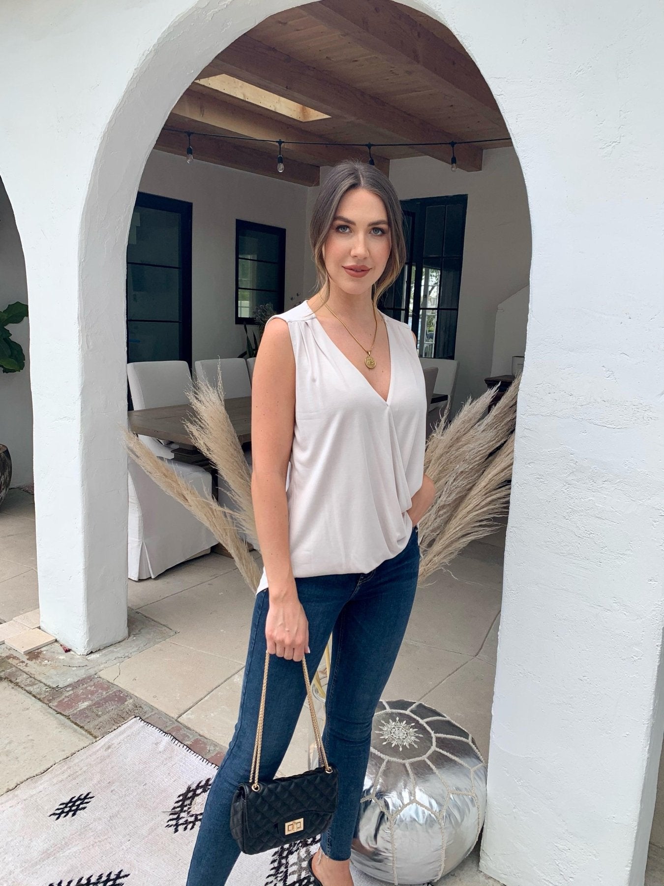 beige sleeveless blouse on woman in dark denim pants holding black purse