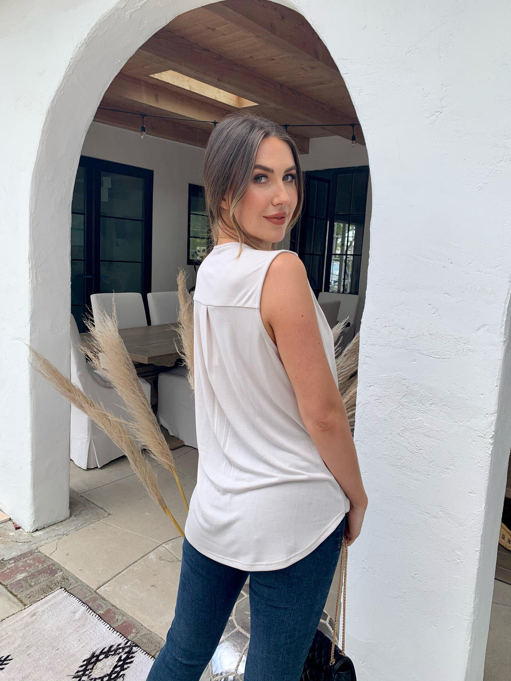 back side of beige sleeveless blouse on woman in dark denim pants